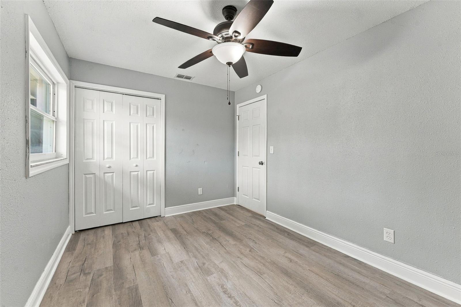 Empty bedroom with wood-look flooring, a ceiling fan, and white double closet doors.