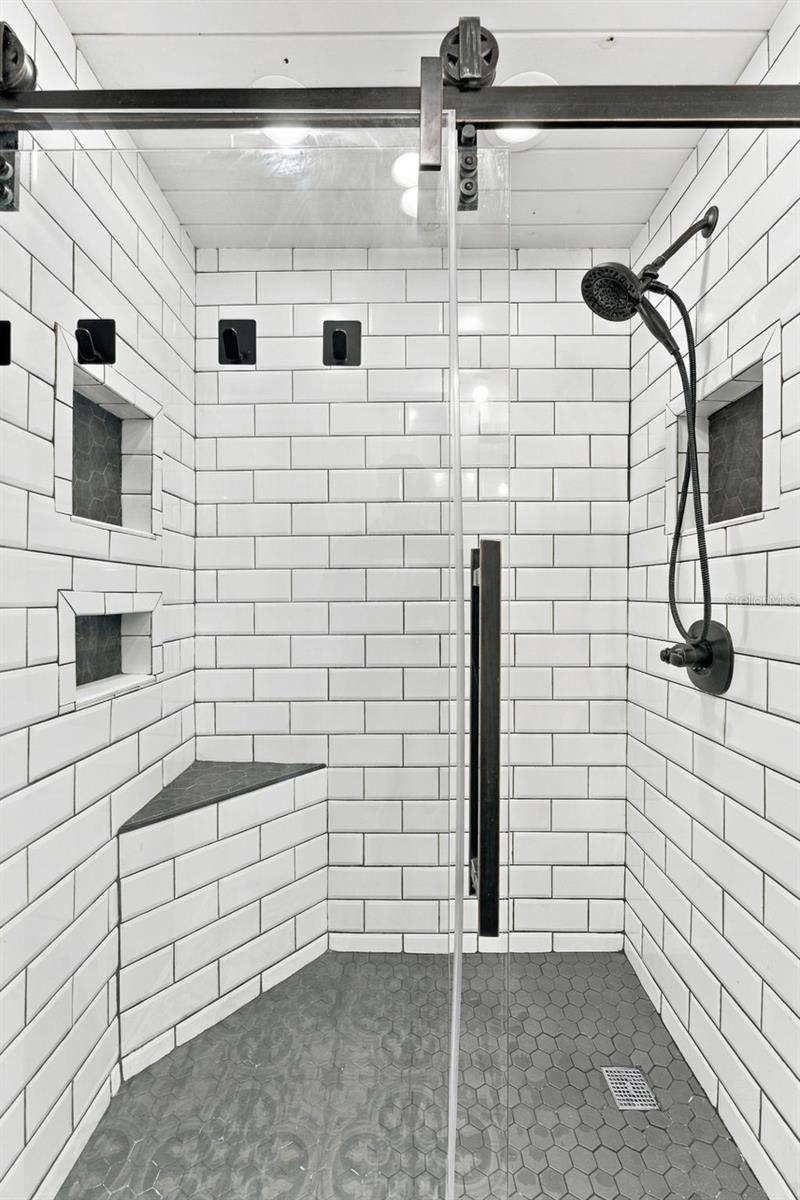 Walk-in shower with white subway tile, gray hexagonal floor, corner bench, and black fixtures.