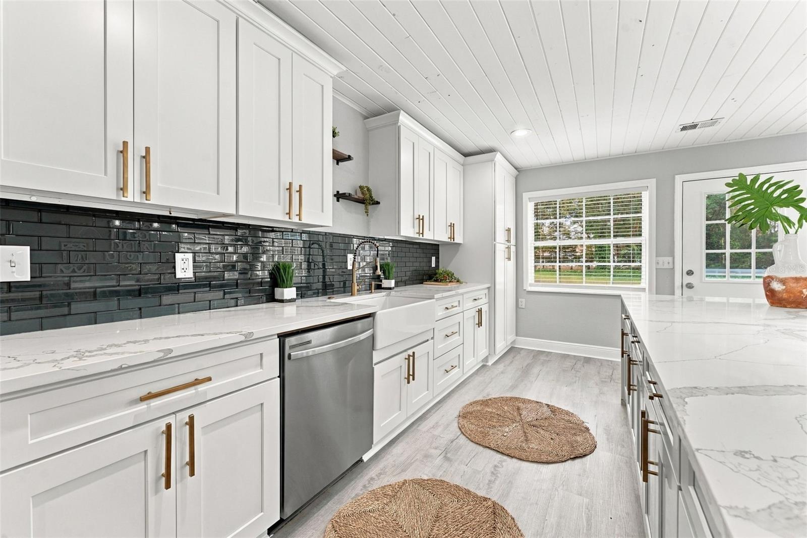 Bright white kitchen with black tile backsplash, marble-look counters, and brass cabinet hardware.