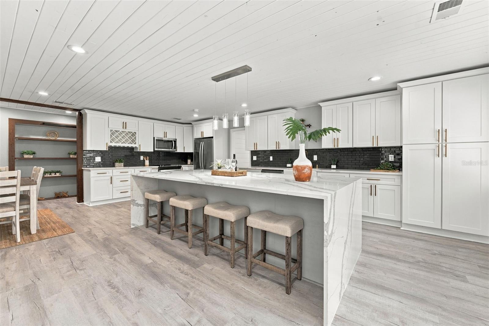 Spacious white kitchen with a large marble-look island, black backsplash, and row of stools.