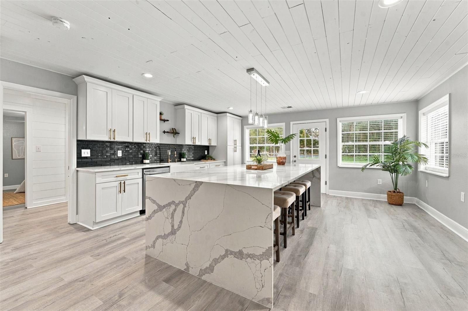 Bright kitchen with a large veined island, white cabinetry, black tile backsplash, and bar stools.