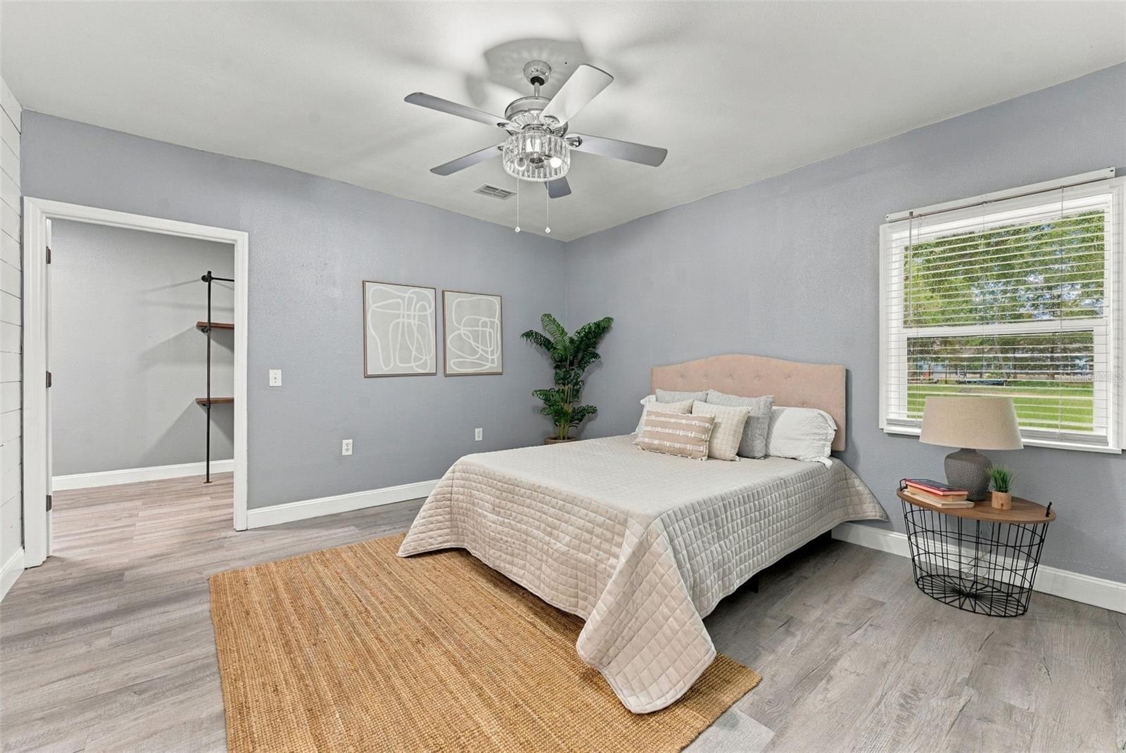 Staged bedroom with a neutral bed, ceiling fan, and open closet doorway.