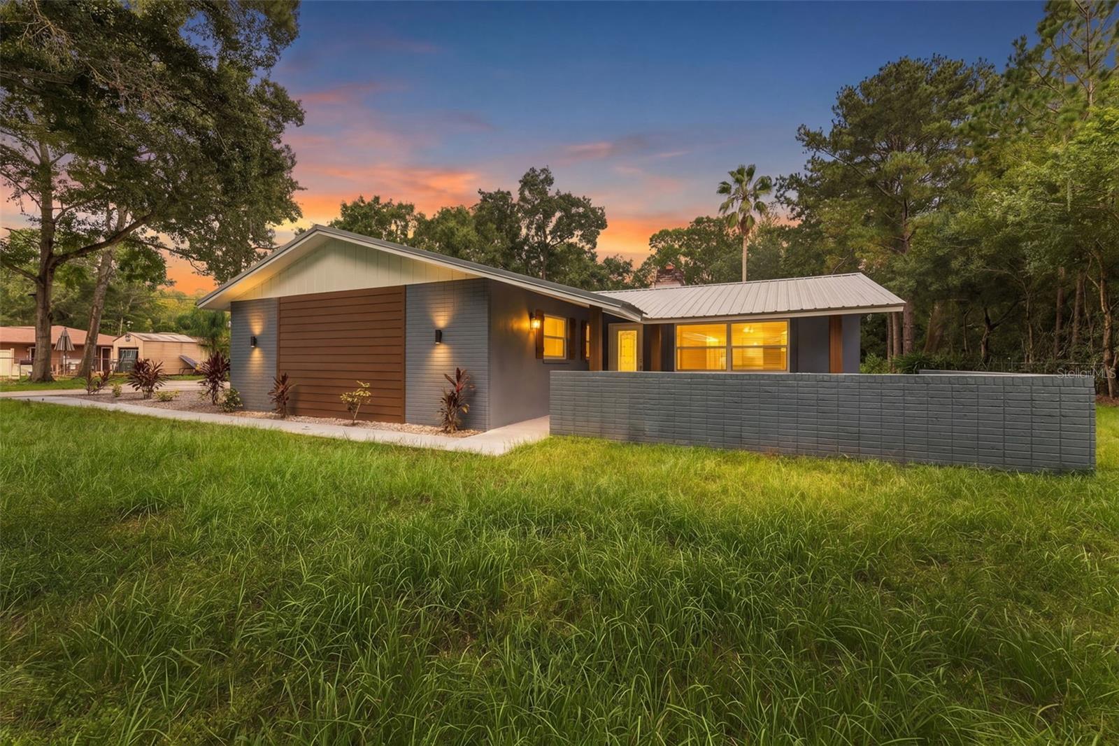 Modern single-story home with a metal roof and low privacy wall at sunset.
