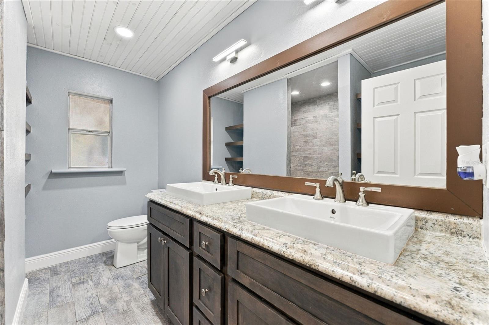 Bathroom with double vessel sinks, a dark wood vanity, and a large framed mirror.
