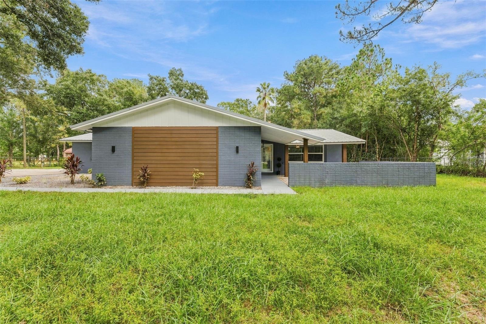 Modern single-story home with blue-gray brick, a wood-slat facade accent, and a broad grassy lawn.