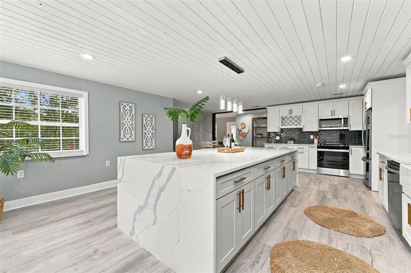 Kitchen with a large veined white island, white cabinetry, and stainless steel appliances.