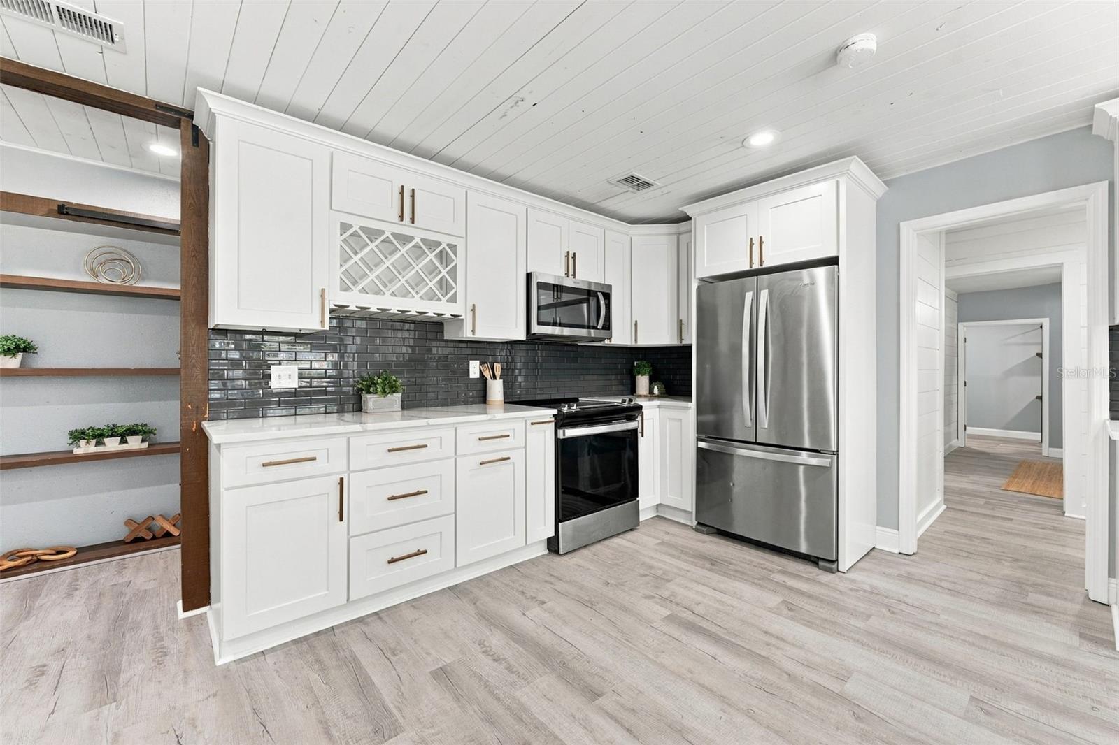 Kitchen with white cabinets, dark tile backsplash, stainless steel appliances, and open wood shelving.