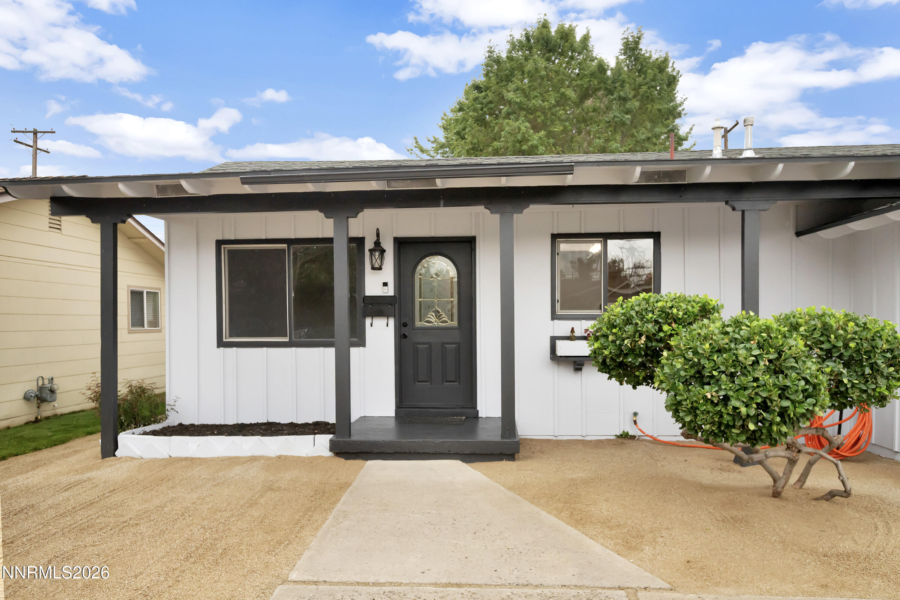 White single-story home with a covered dark-trimmed porch and decorative-glass front door.