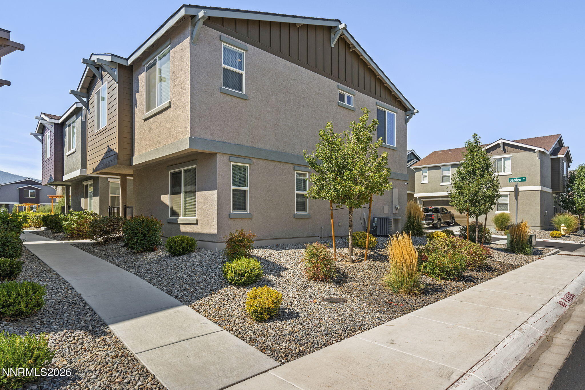 Two-story stucco townhouse with dark gables, gravel landscaping, and sidewalks.
