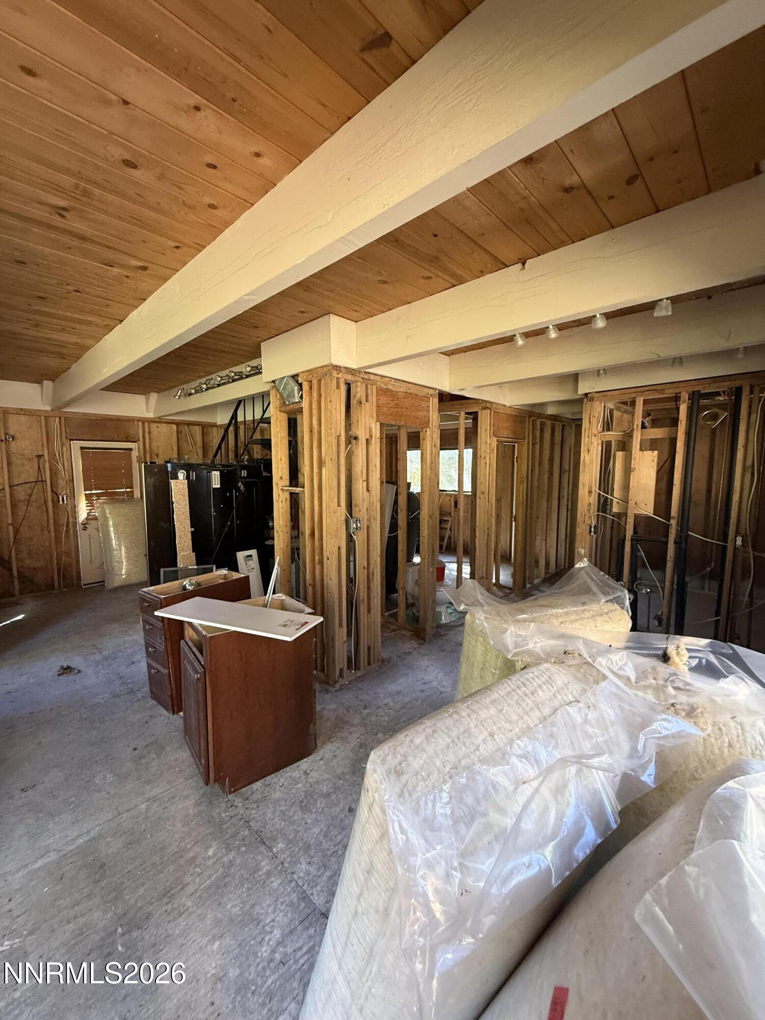 Unfinished interior with exposed framing, a wood-plank ceiling, and wrapped insulation on the floor.