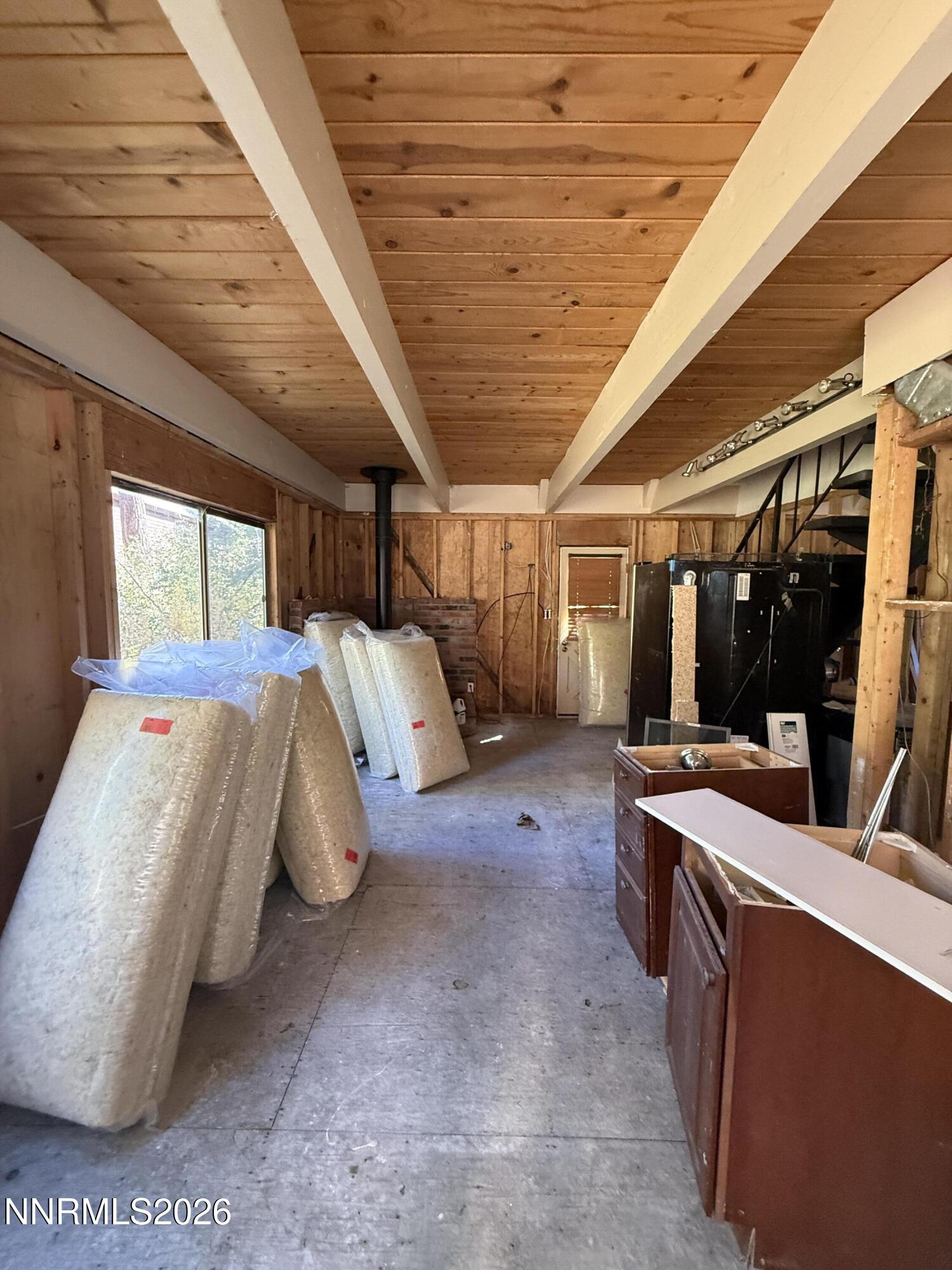 Unfinished garage with exposed framing, renovation materials, and appliances.