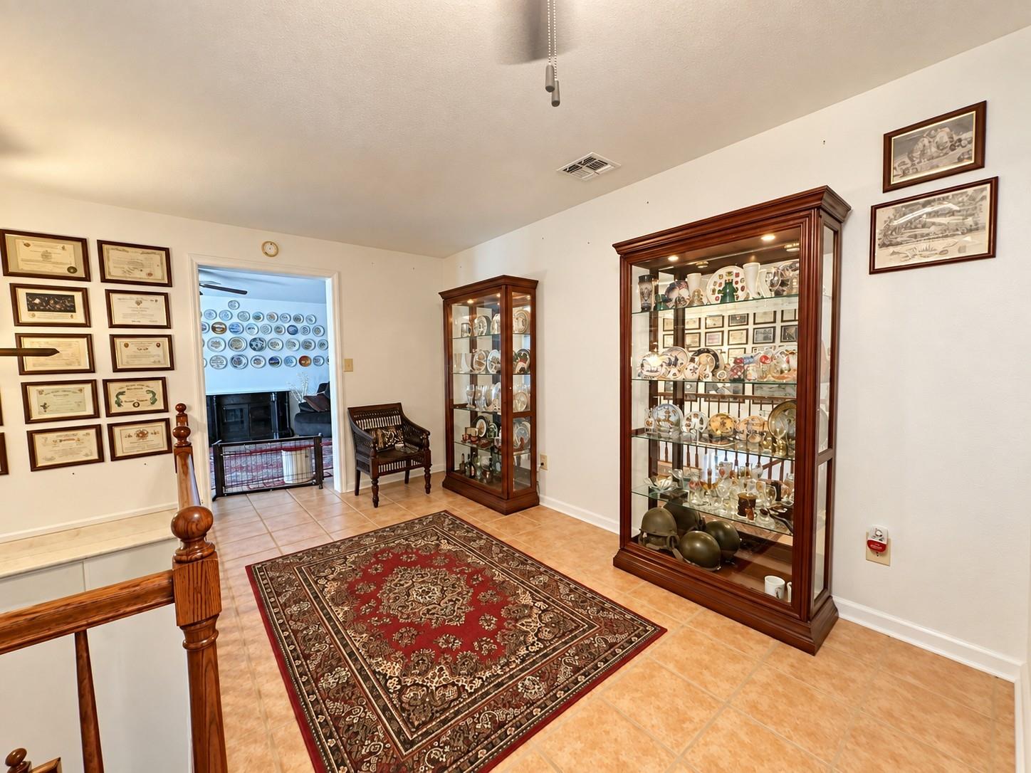 Hallway with glass-front cabinets displaying plates and collectibles beside a patterned rug.