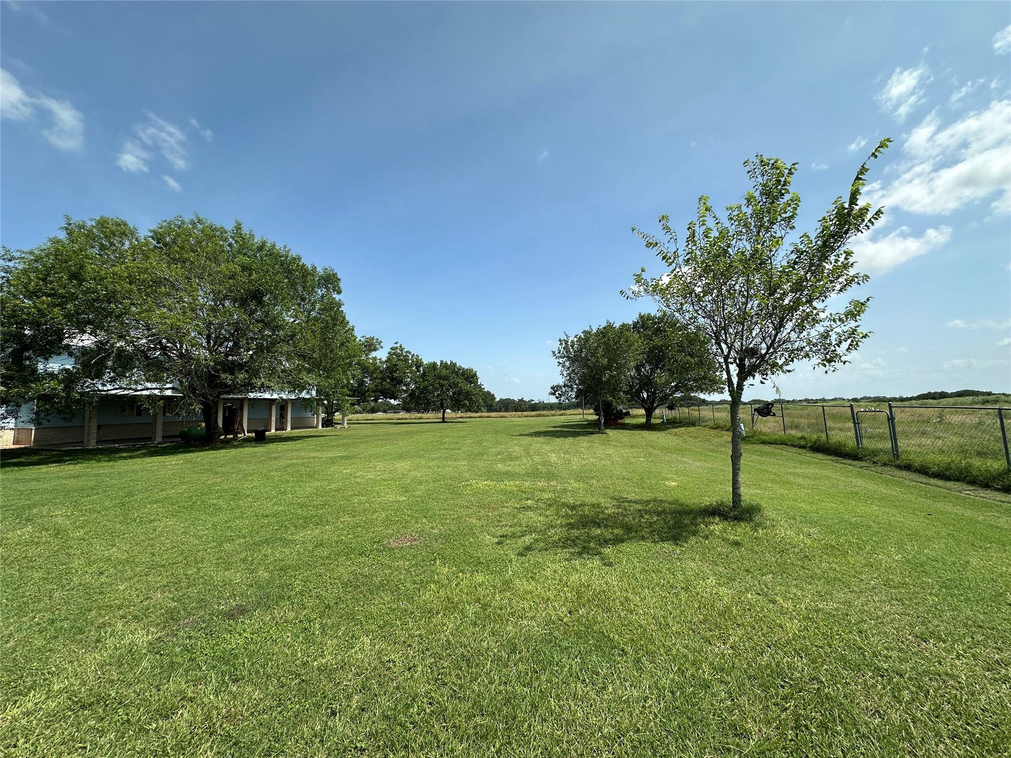 Expansive lawn with shade trees, a fenced pasture, and a single-story home nearby.