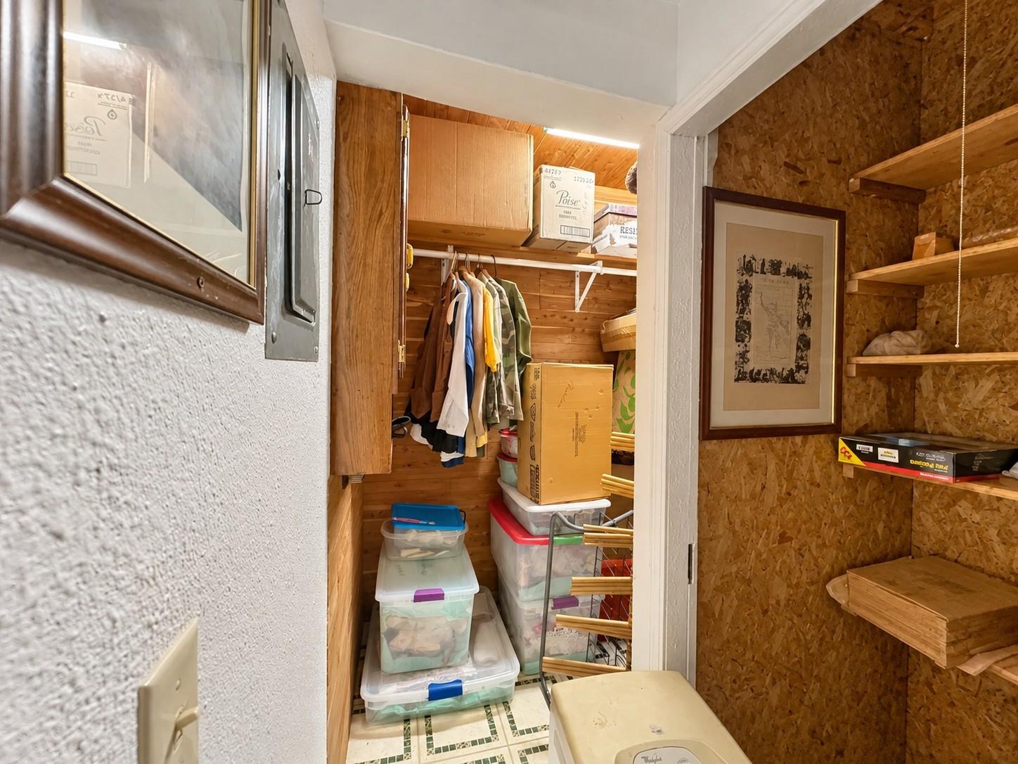 Crowded storage closet with hanging clothes, stacked bins, and open shelves.