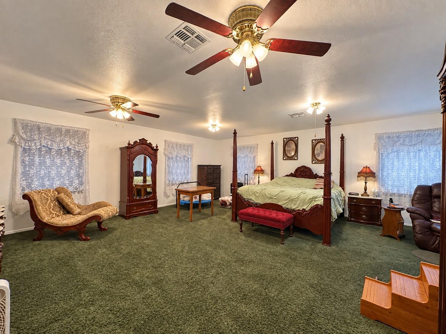 Furnished bedroom with a four-poster bed, green carpet, and two ceiling fans.