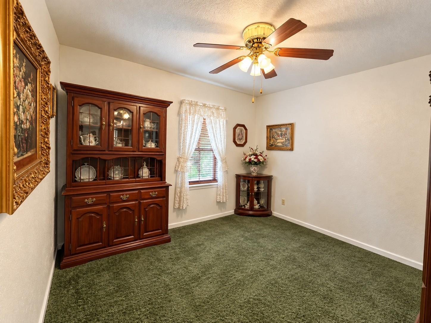 Carpeted room with a dark wood china cabinet, corner curio cabinet, and ceiling fan.