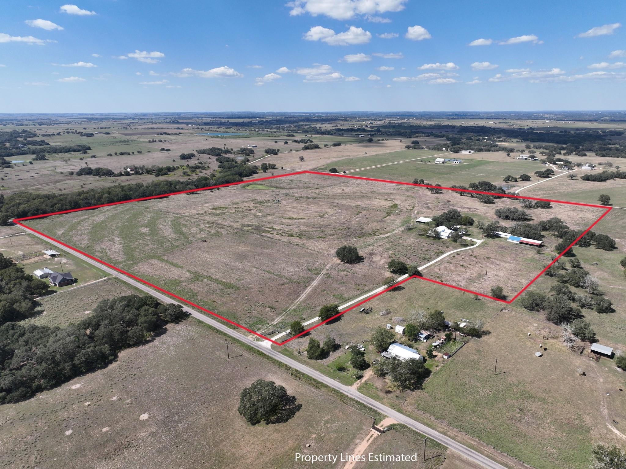 Aerial view of open rural acreage outlined in red, with scattered trees, farm buildings, and a road.
