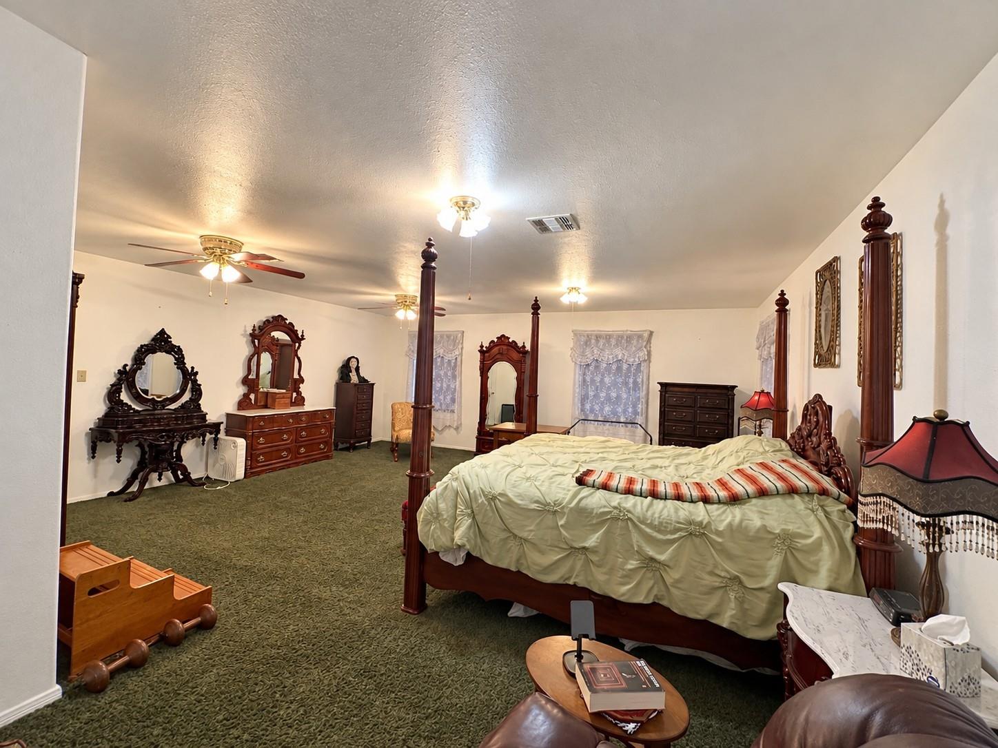 Spacious bedroom with a dark wood four-poster bed, ornate dressers, and green carpet.