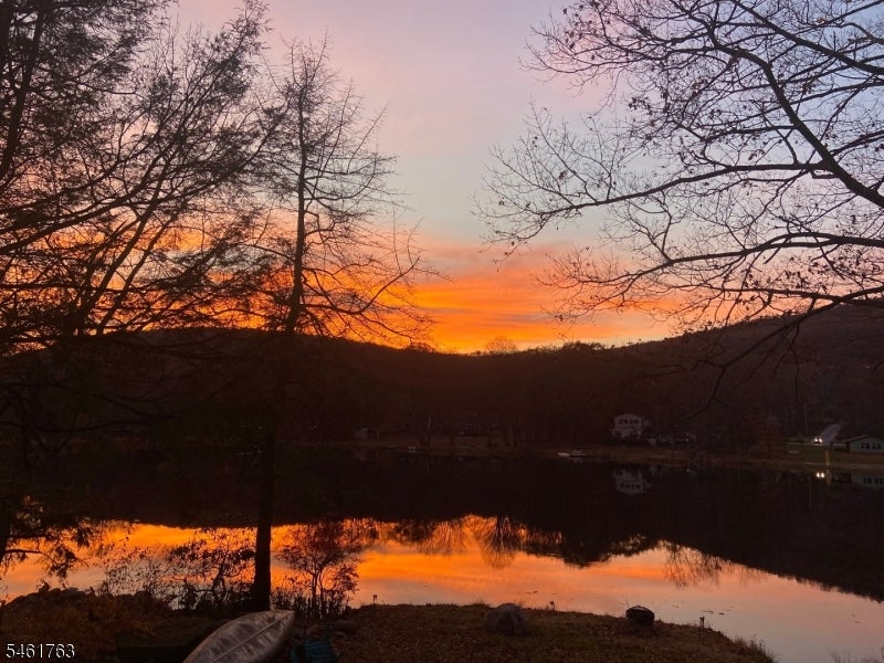 Lake at sunset, framed by bare trees, with wooded hills and reflections on the water.