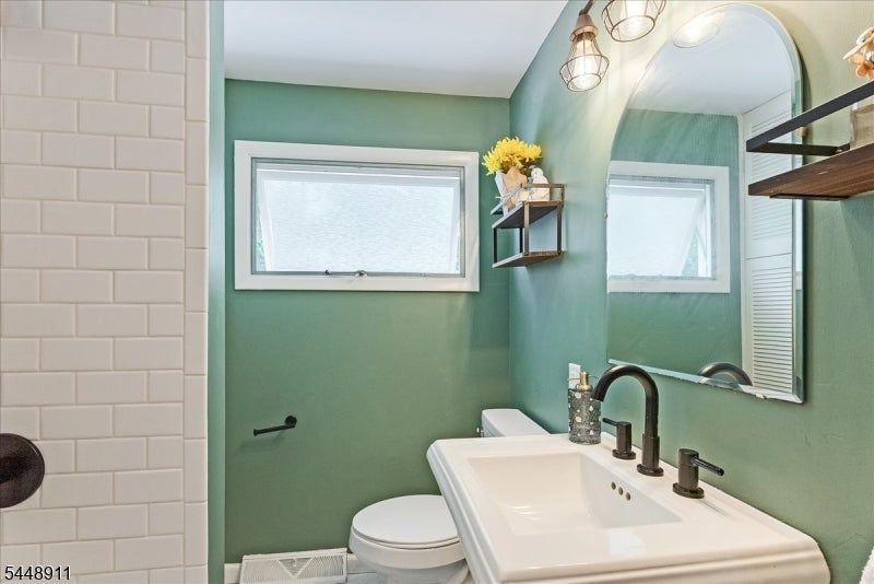 Bathroom with green walls, white subway-tile shower, arched mirror, and dark vanity faucets.