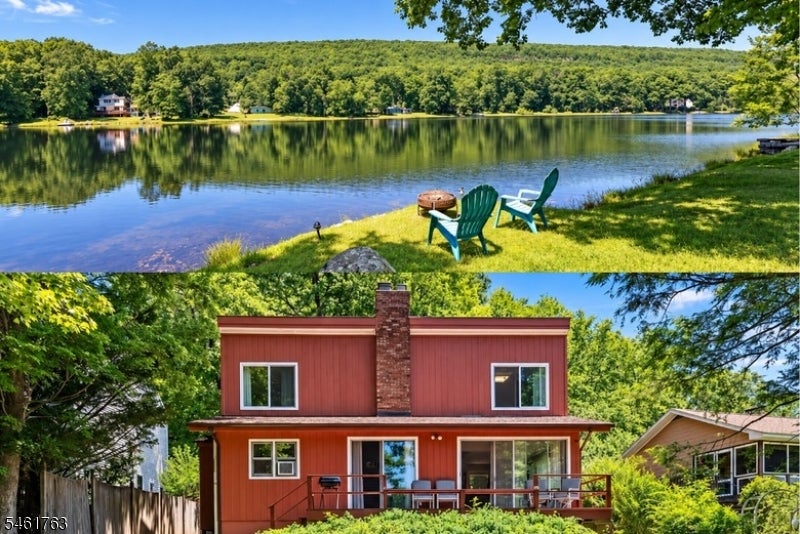 Red two-story house with a deck beside a calm, wooded lake.