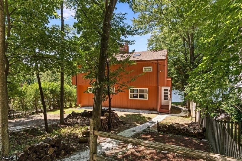 Orange two-story home among mature trees, with a gravel path and a glimpse of the lake.