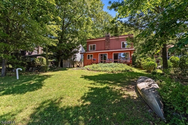 Red two-story house with a raised deck on a wooded, grassy lot; a canoe lies in the foreground.