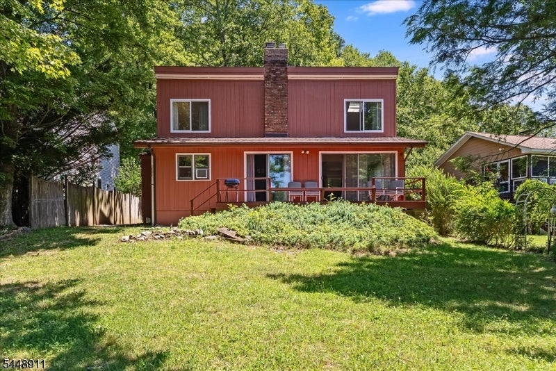 Two-story reddish-brown home with a covered rear deck, brick chimney, and grassy yard.