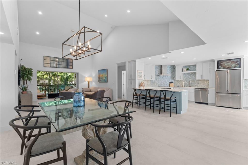 Open-plan kitchen and dining area with a blue island, glass table, and vaulted ceiling.