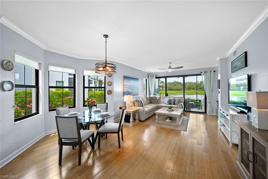 Open living and dining room with a sectional sofa and windows overlooking a lawn and water.