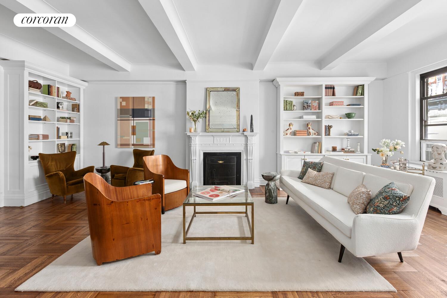 Staged living room with a white sofa, built-in bookshelves, ornate fireplace, and herringbone floors.