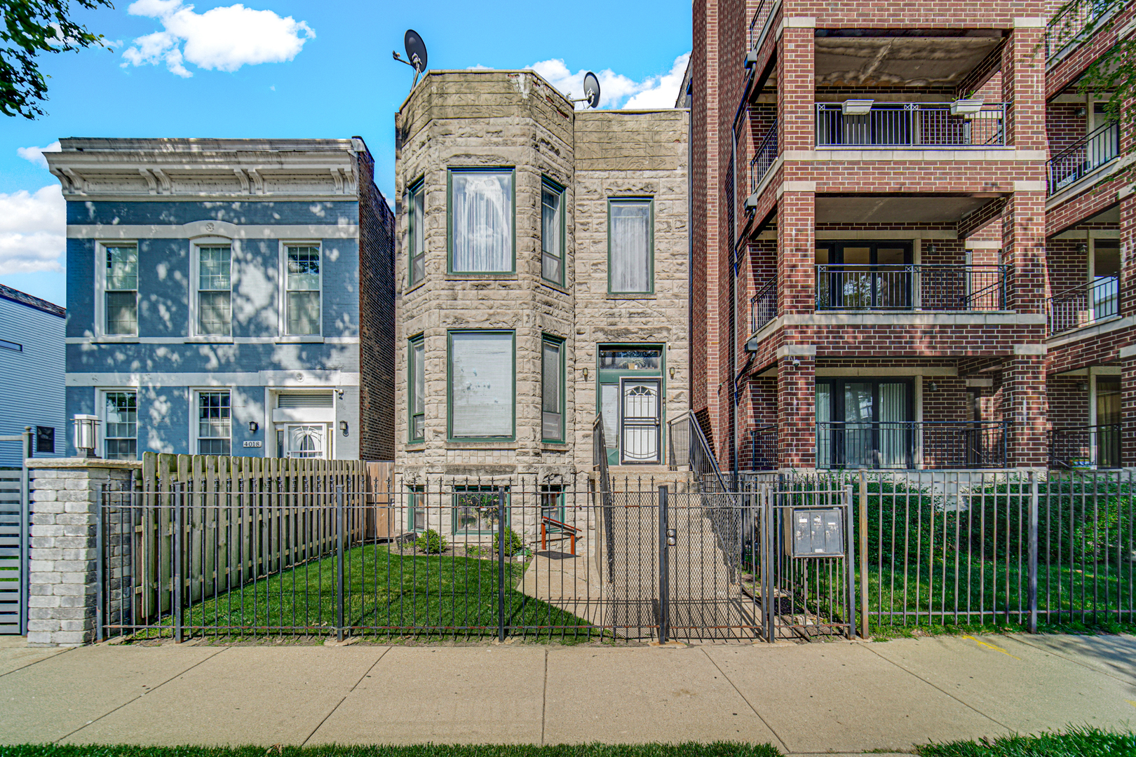 Narrow stone Chicago home between a blue house and brick apartment building, with a fenced front yard.