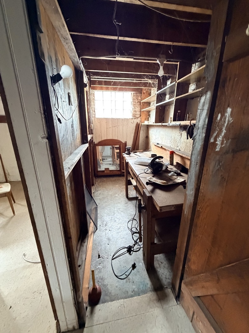 Narrow workshop with exposed wood framing, open shelves, and a tool-covered workbench.