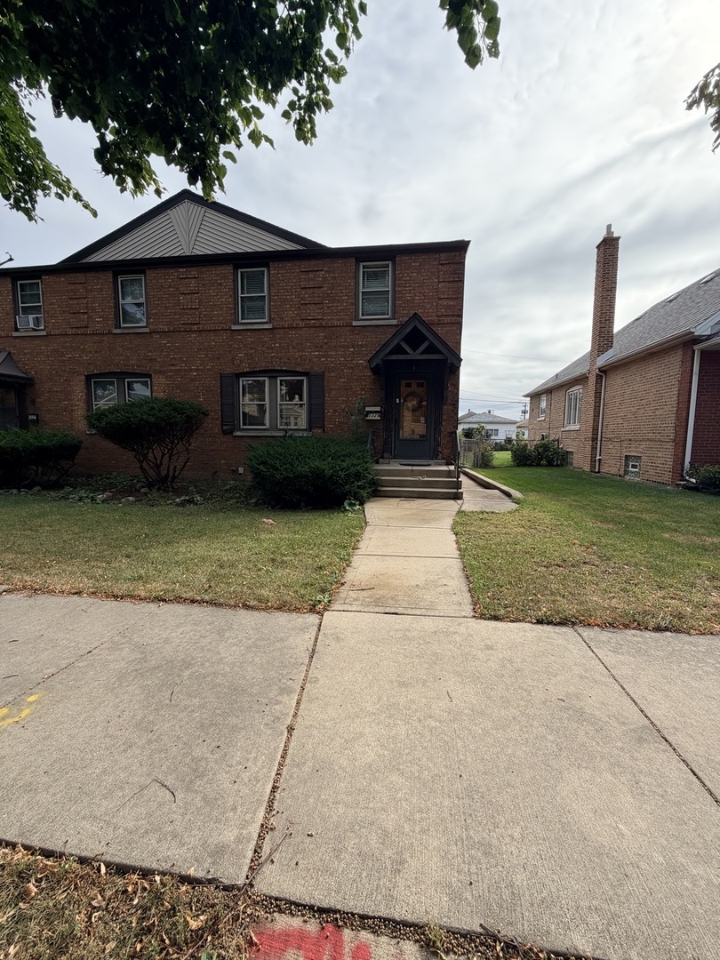Two-story brick home with a gabled roof, front lawn, and walkway to the entry.
