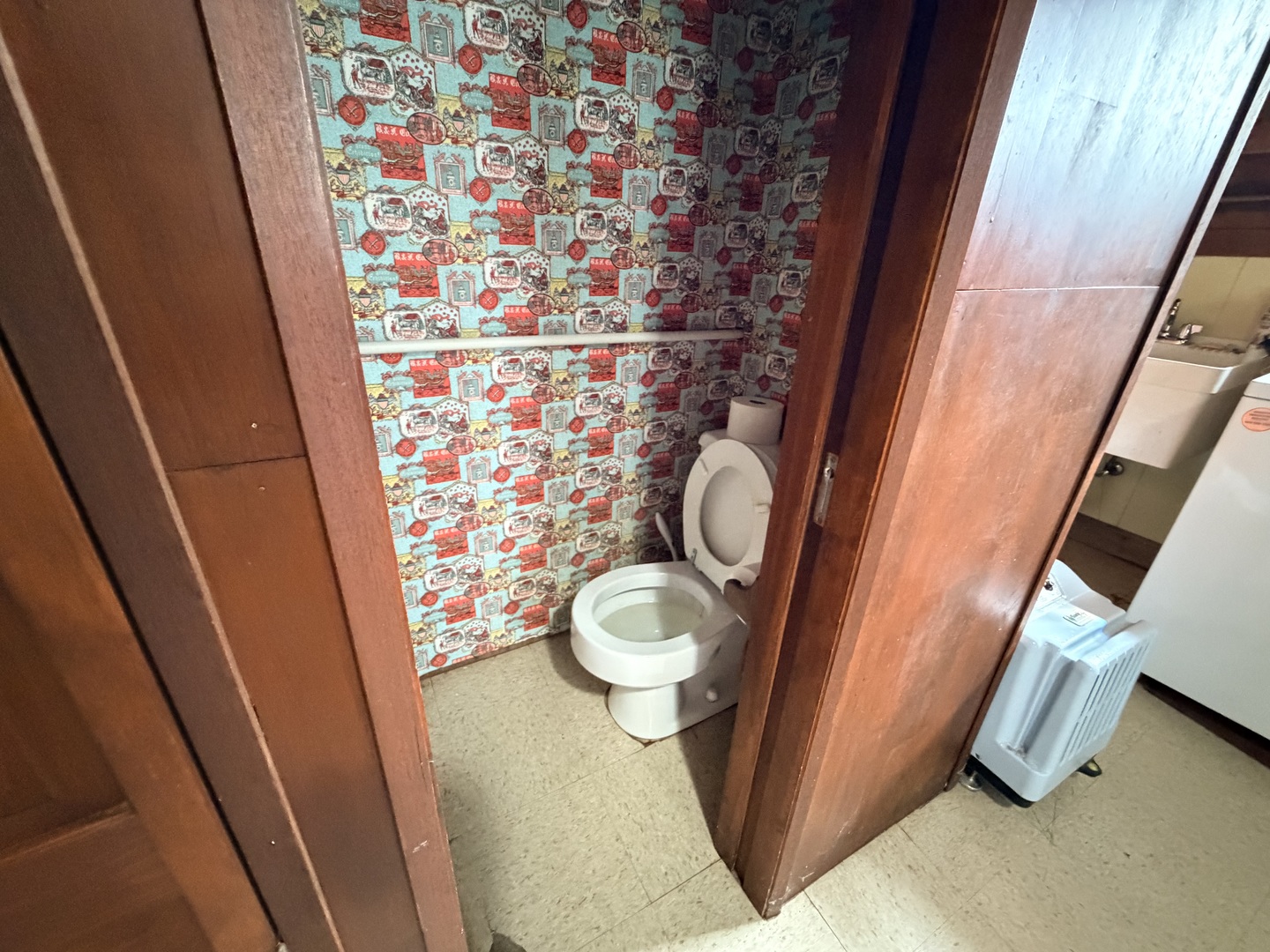 Small bathroom with a white toilet, colorful patterned wallpaper, and wooden doorways.