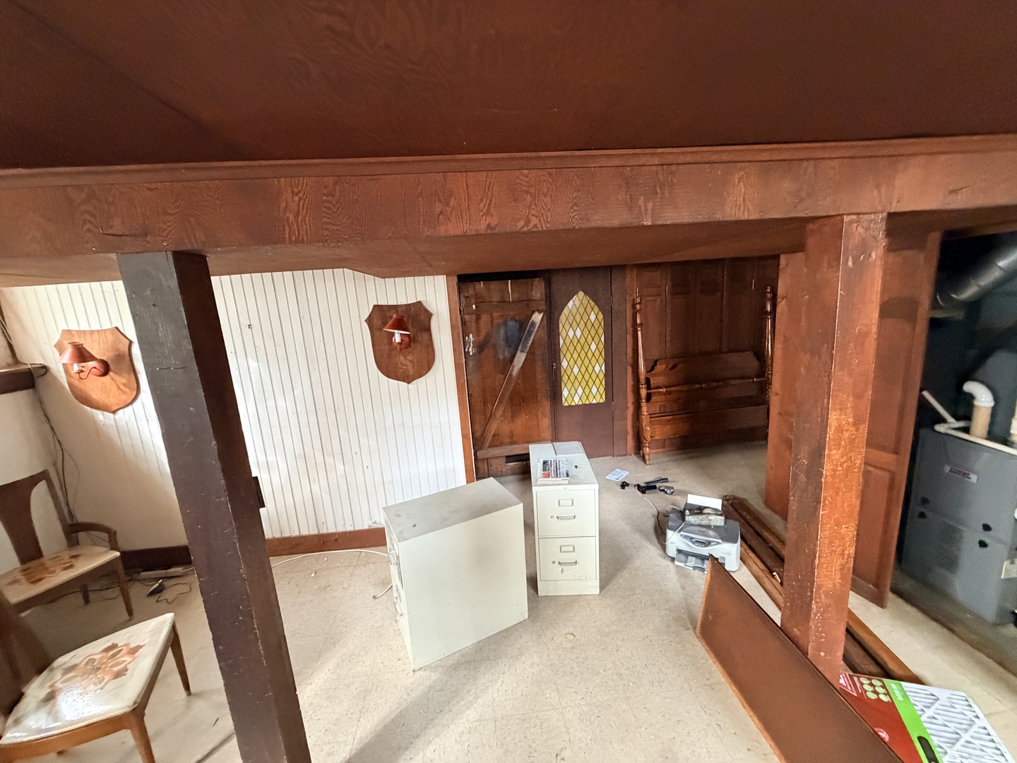 Basement with a low wood-beam ceiling, paneled walls, old furniture, and filing cabinets.