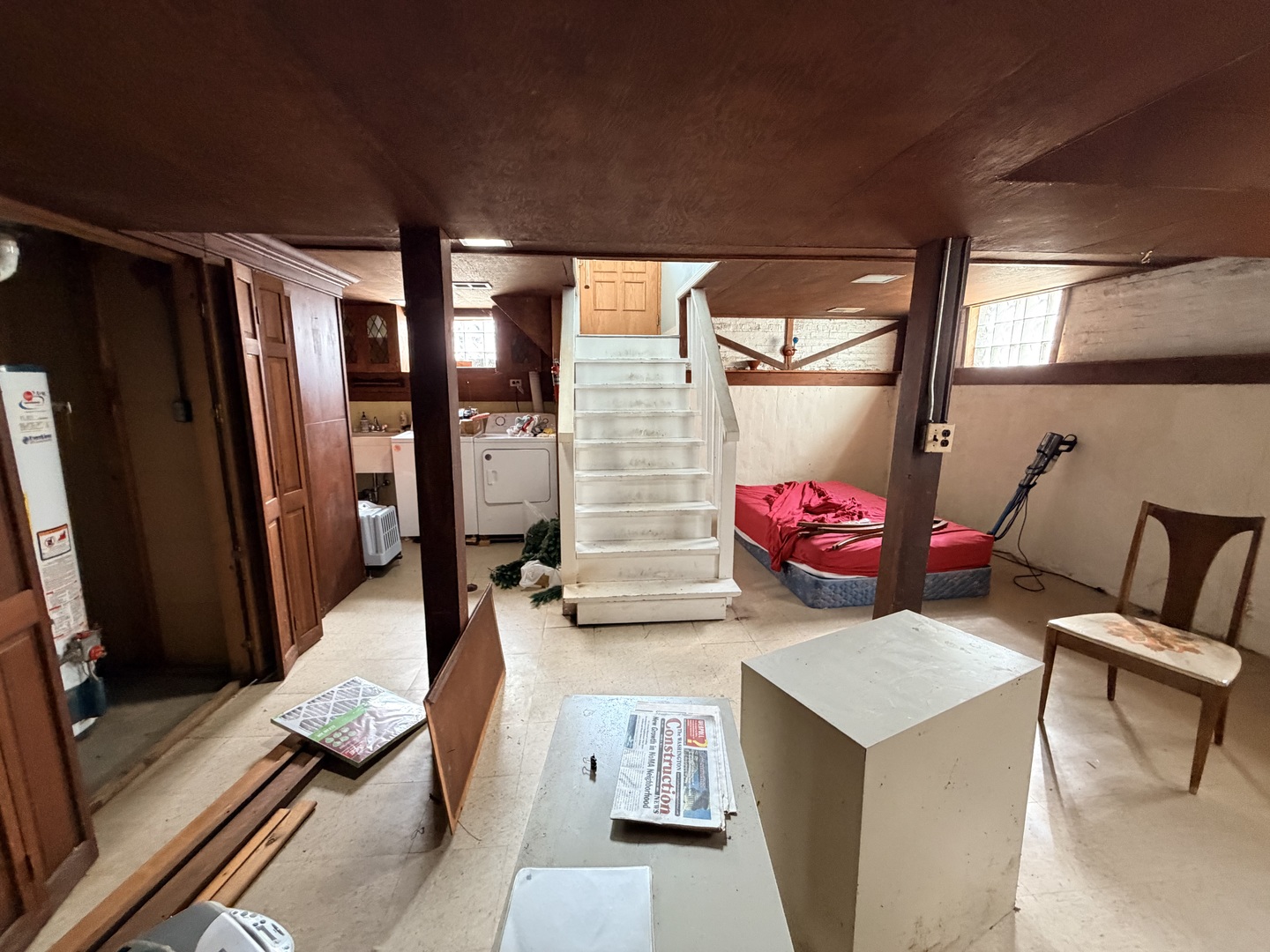Basement with a low ceiling, central staircase, laundry appliances, and a mattress.
