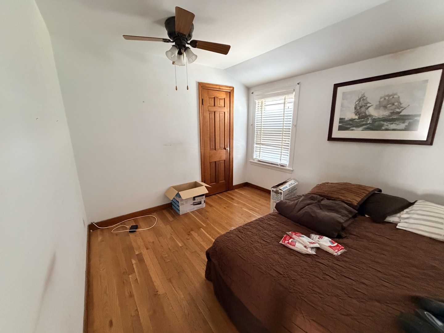 Bedroom with hardwood floors, a large bed, ceiling fan, and framed ship painting.