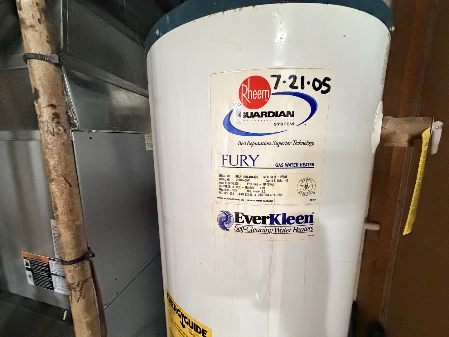 Rheem gas water heater beside a furnace, with its product labels visible.