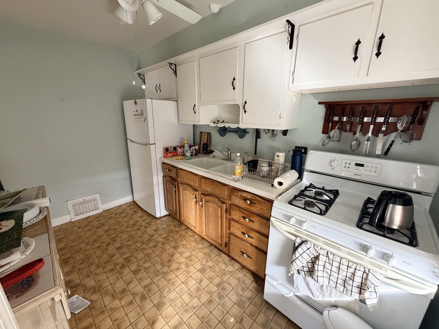 Kitchen with white cabinets, wood lower cabinets, a gas range, and tan tile flooring.