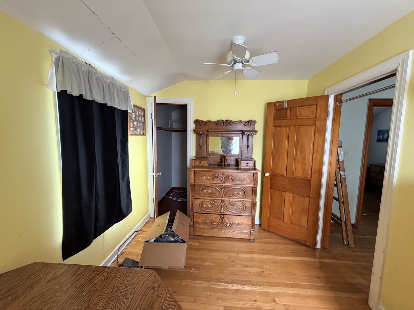 Bedroom with yellow walls, hardwood floors, and an ornate wooden dresser beneath a ceiling fan.