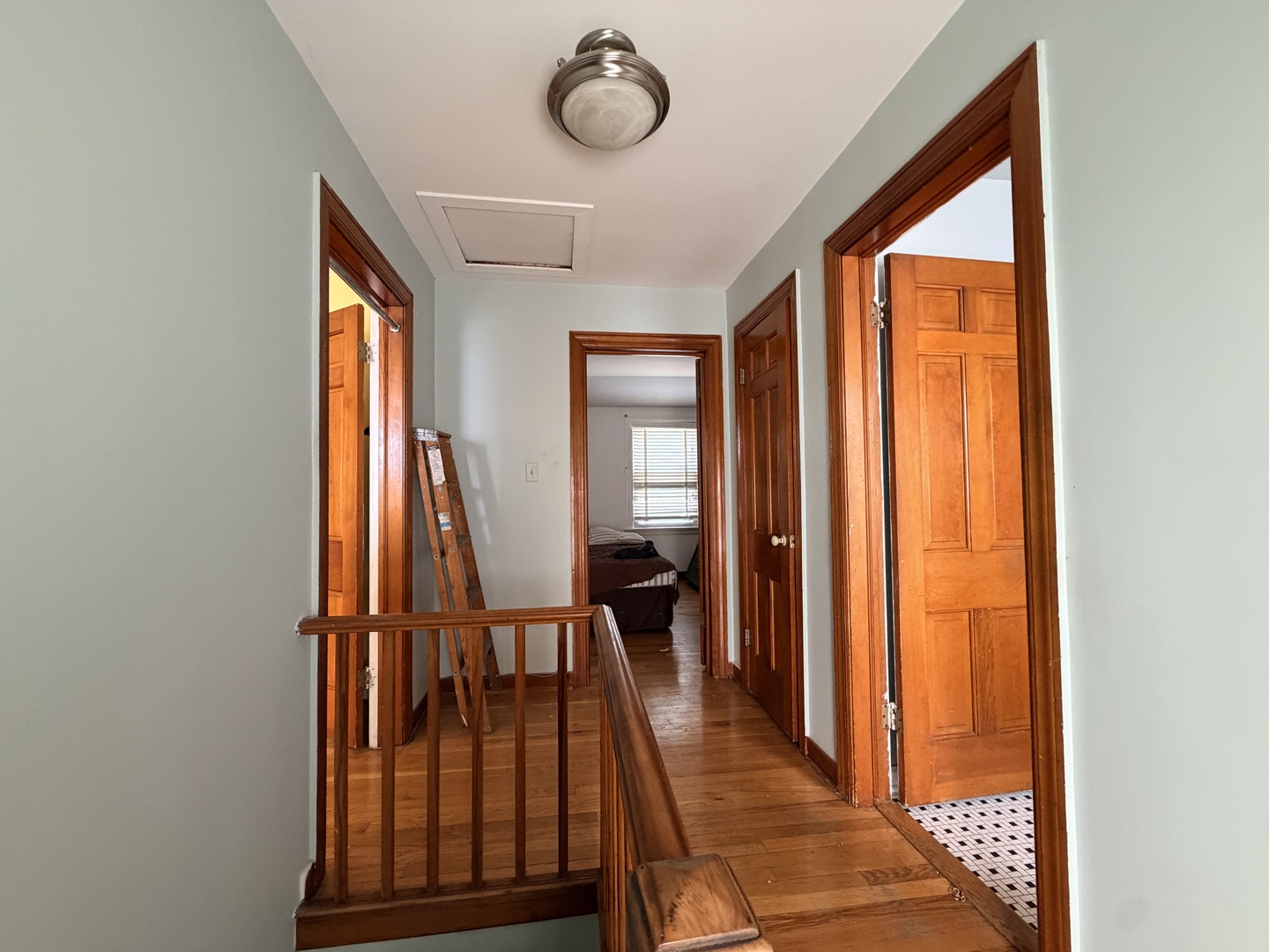 Hallway with hardwood floors, wood-trimmed doorways, and a wooden stair railing.