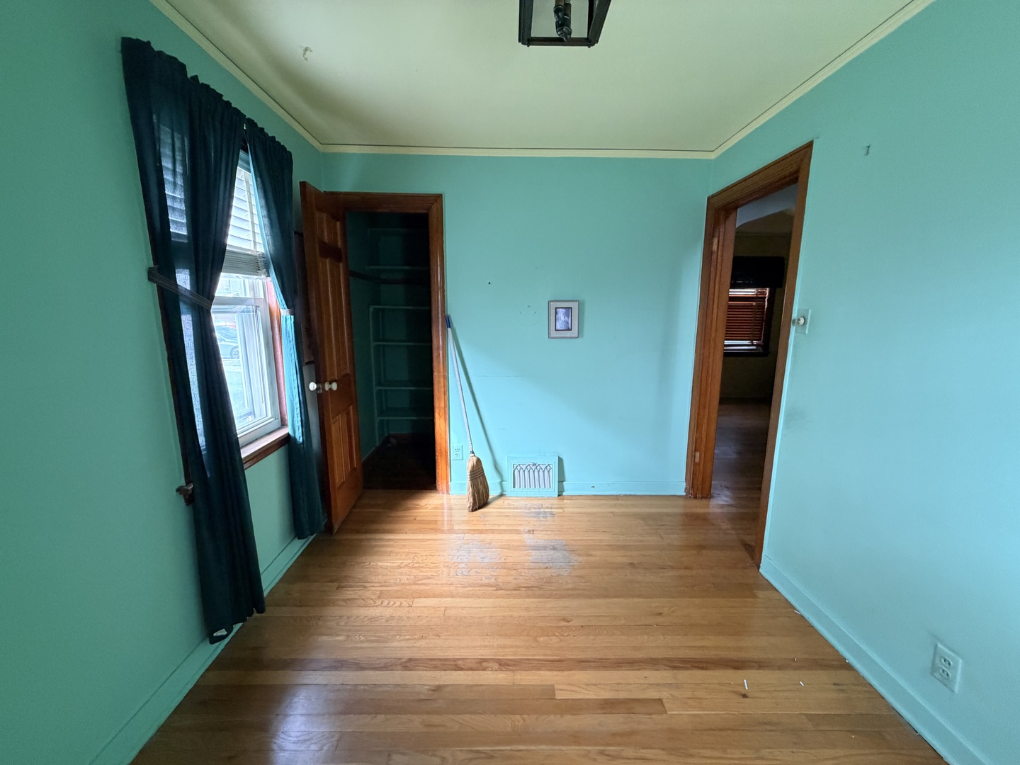 Empty turquoise room with hardwood floors, dark window curtains, and an open closet.