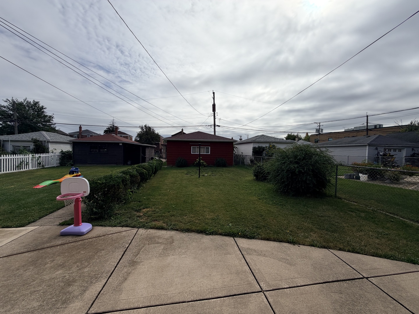 Backyard with a concrete patio, trimmed hedges, and a child-sized basketball hoop.