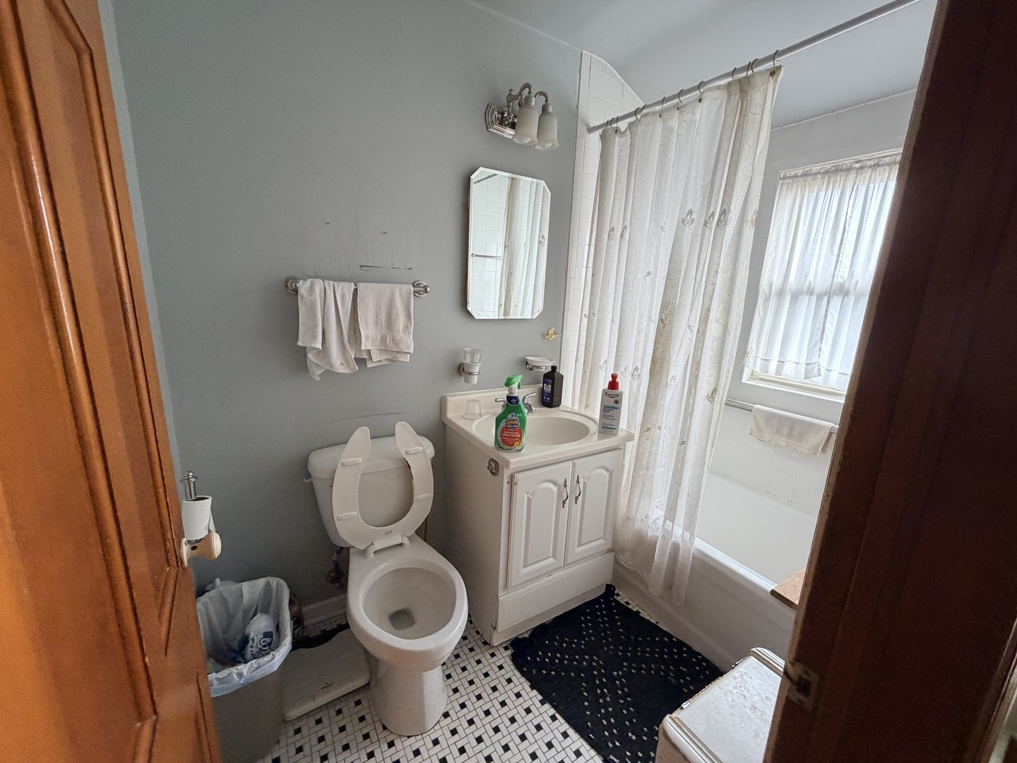 Bathroom with white vanity and toilet, curtained bathtub, and black-and-white mosaic tile floor.