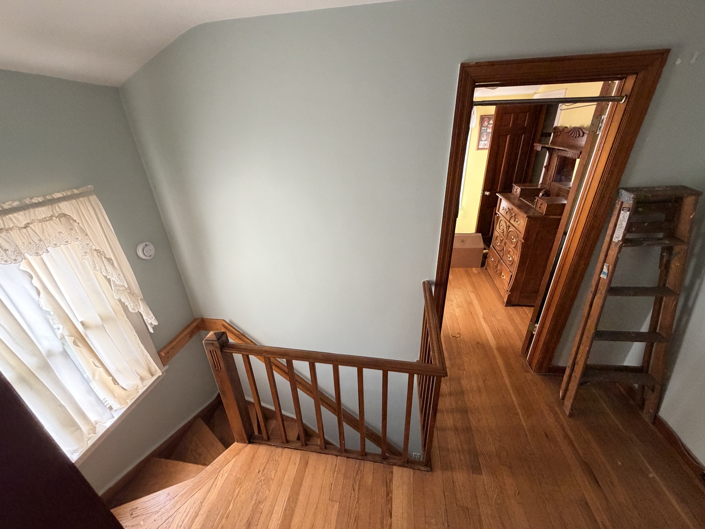 Upstairs landing with a wooden staircase, hardwood floors, and an open doorway to a furnished room.
