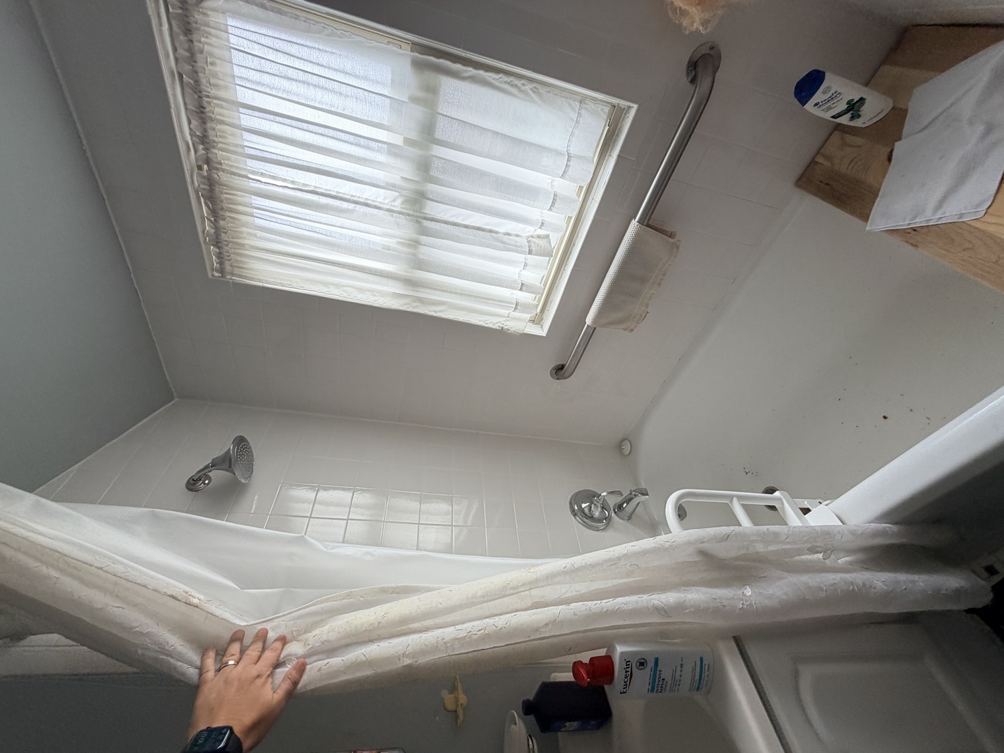 Tiled bathtub and shower with a window, grab bars, and a white curtain.