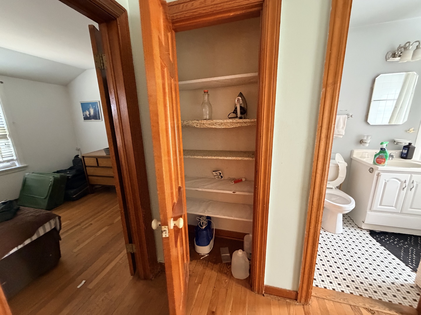 Open built-in closet with multiple shelves between a hardwood-floored bedroom and tiled bathroom.