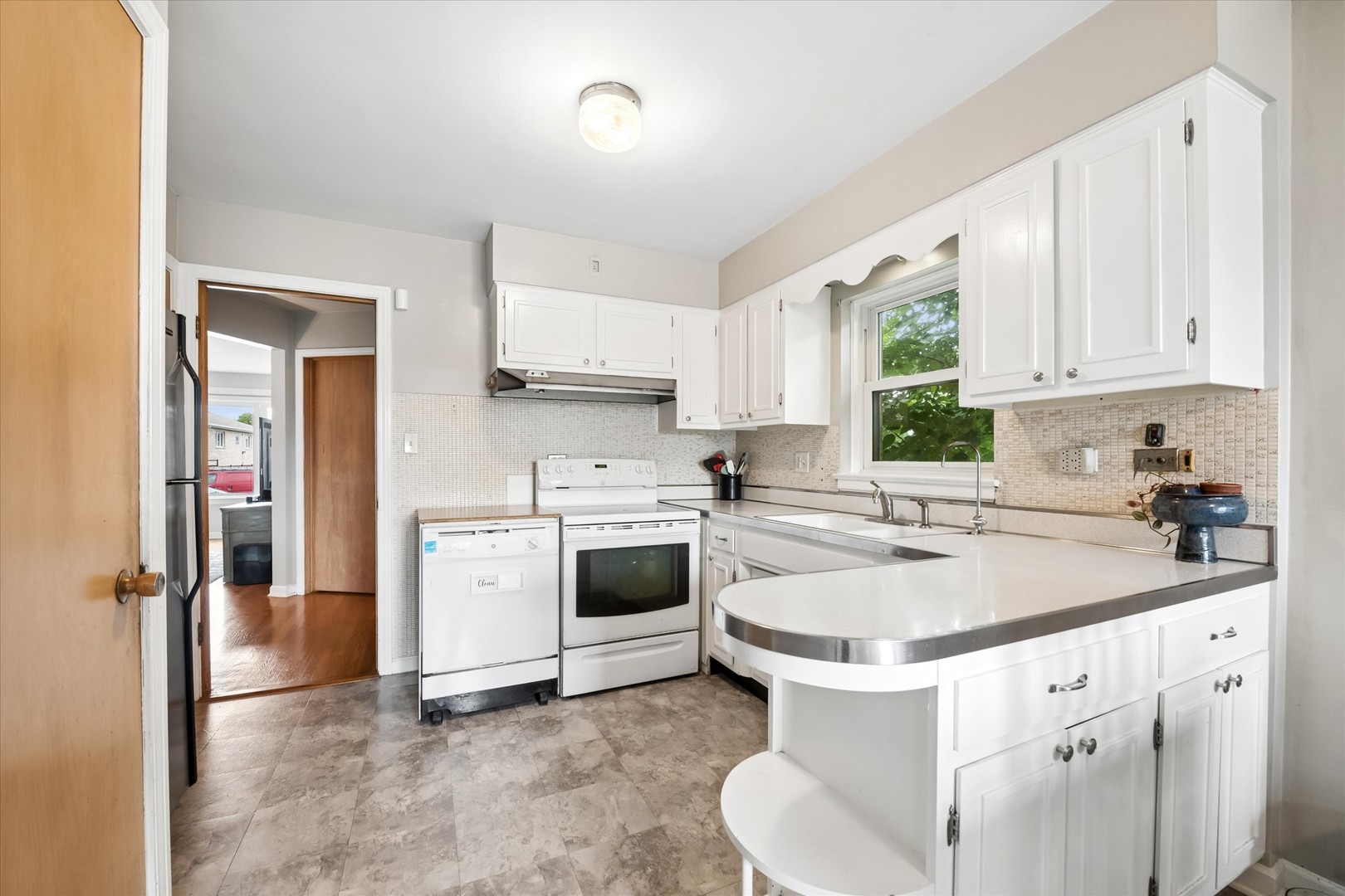Kitchen with white cabinets, a rounded peninsula, tiled backsplash, and a window above the sink.