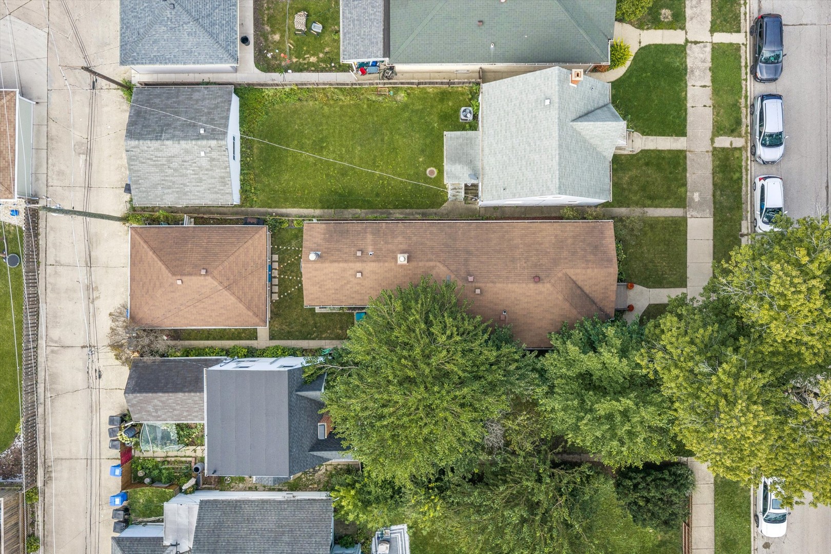Aerial view of a Chicago home with a long brown roof, grassy yard, and mature trees.